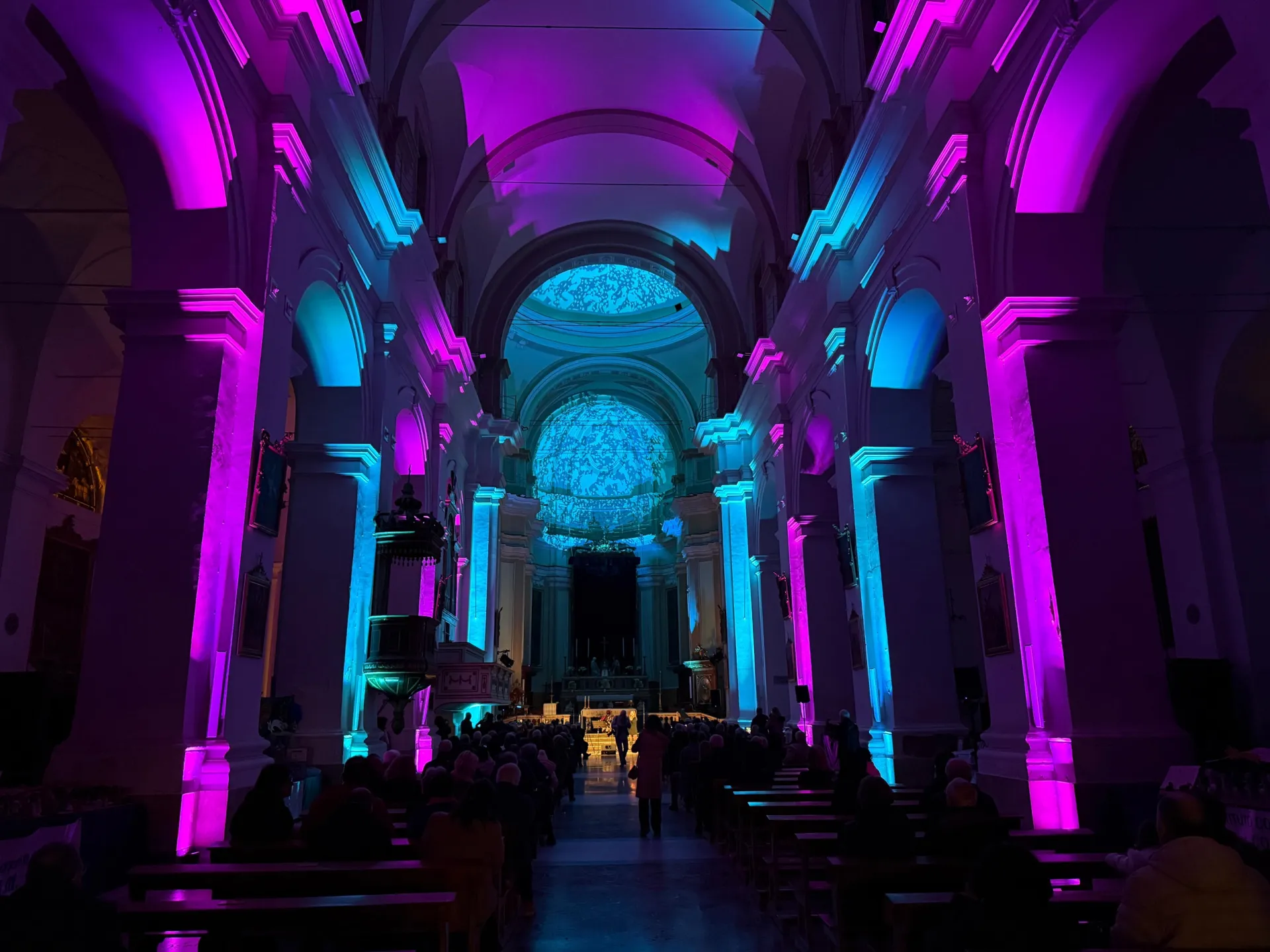 Illuminazione architetturale della navata di una chiesa in toni viola e azzurro durante un concerto