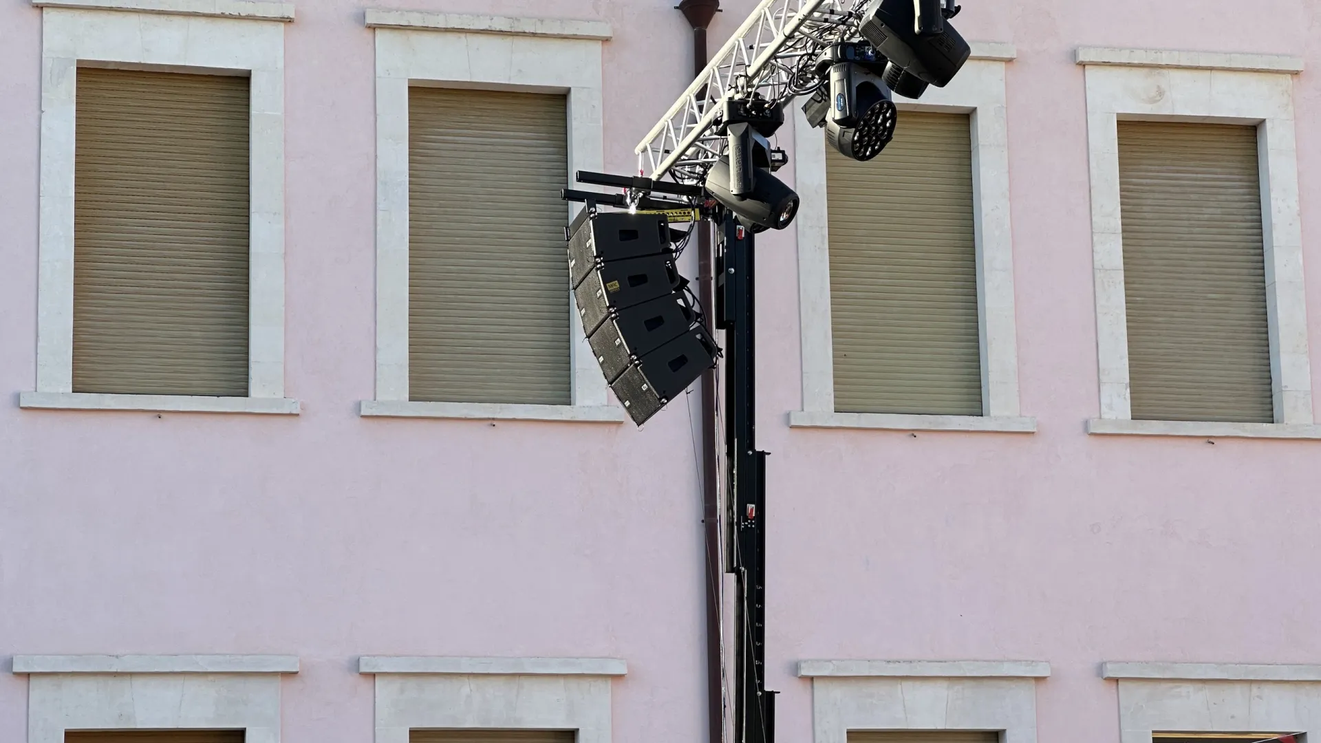 Torre di rigging con impianto audio line array e fari motorizzati a ridosso di una facciata