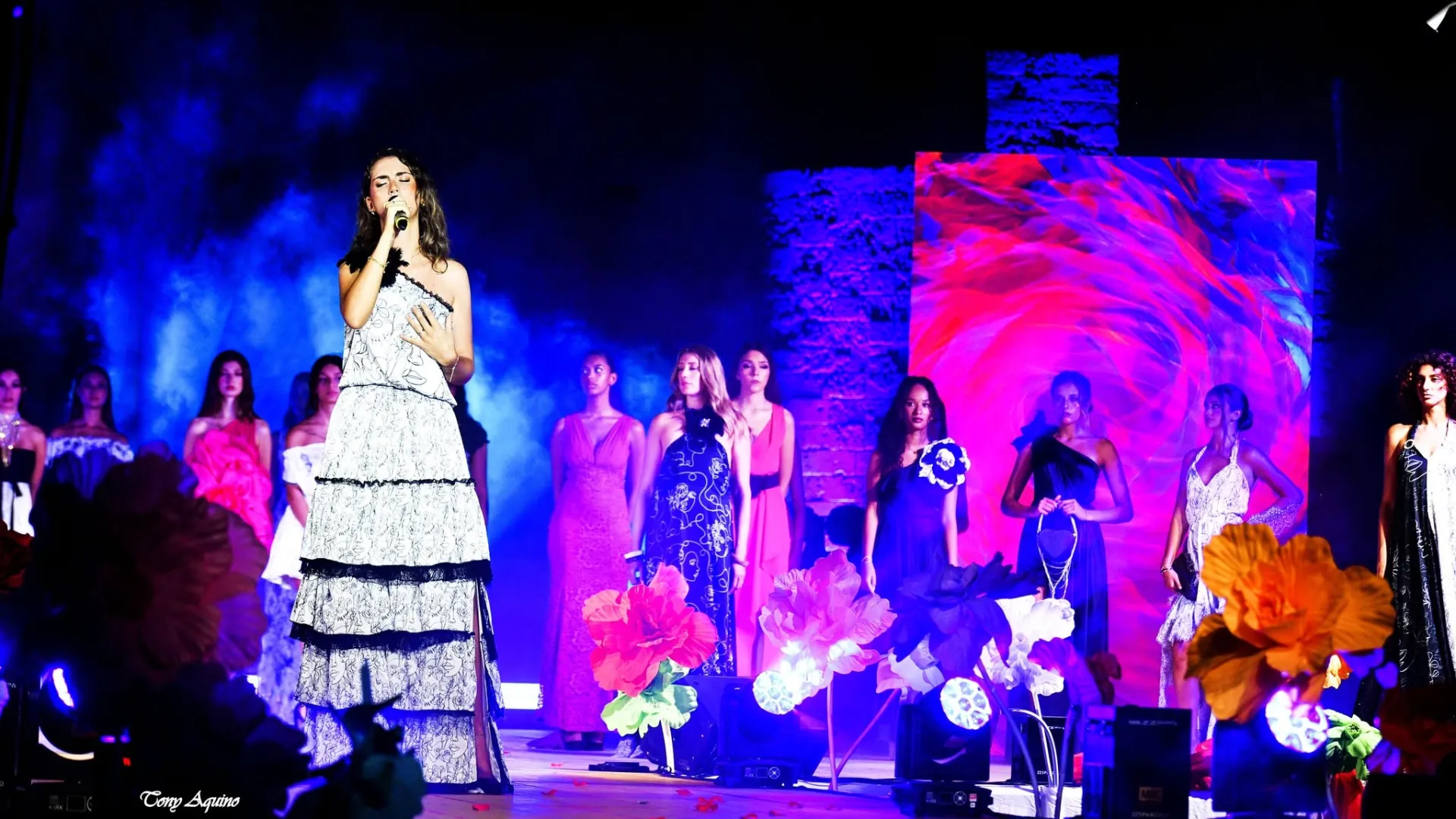Cantante sul palco di una sfilata, con le modelle schierate e un ledwall alle spalle